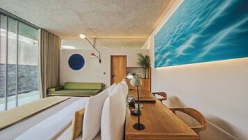 Interior moderno com mesa de jantar de madeira, sofá verde e uma grande janela com vista para a água.
