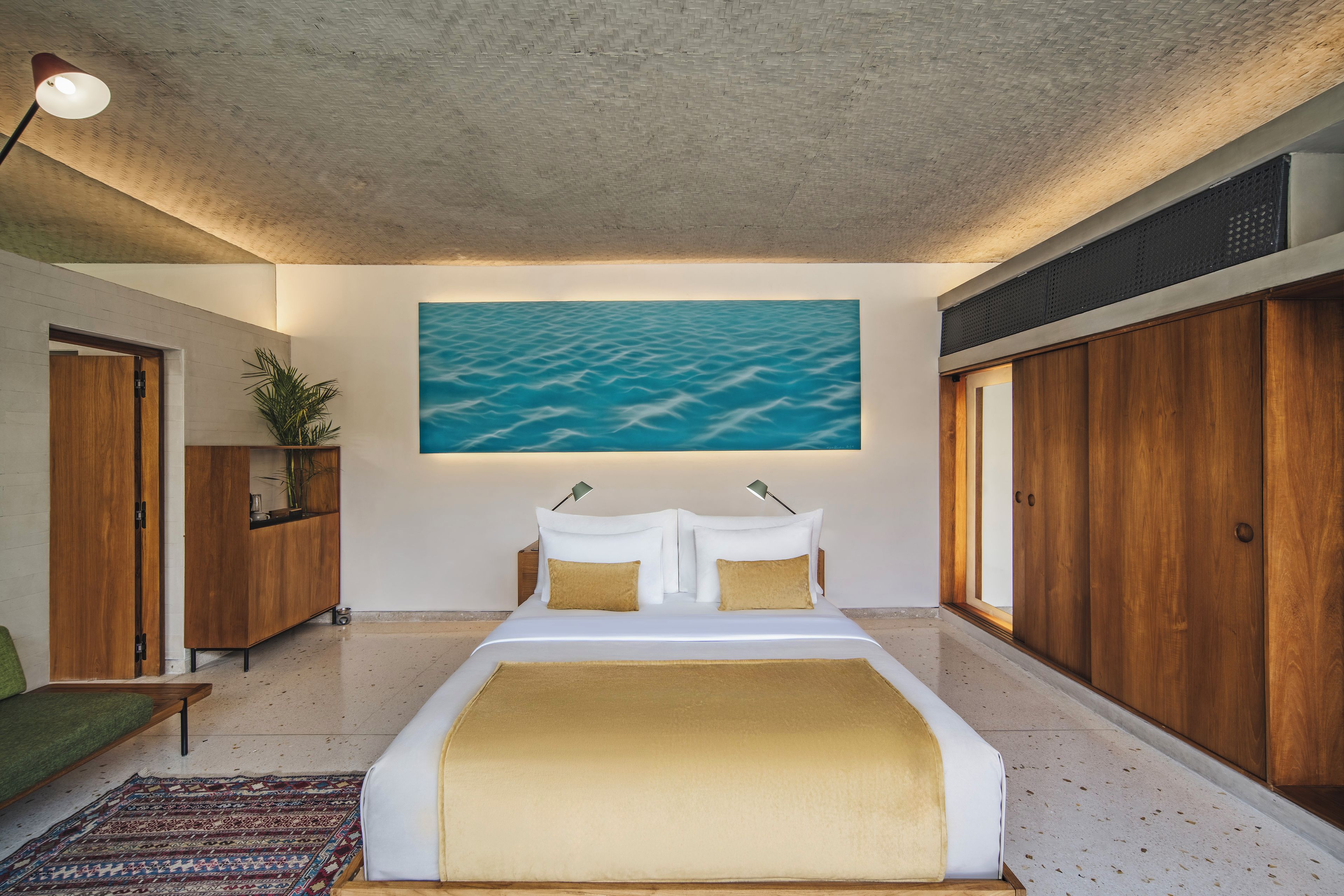 Ein Schlafzimmer mit einem großen Bett, einem Meeresbild, Holzmöbeln und Blick auf den Strand.