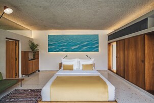 A bedroom with a large bed, a painting of the sea, wooden furniture, and a view of the beach.