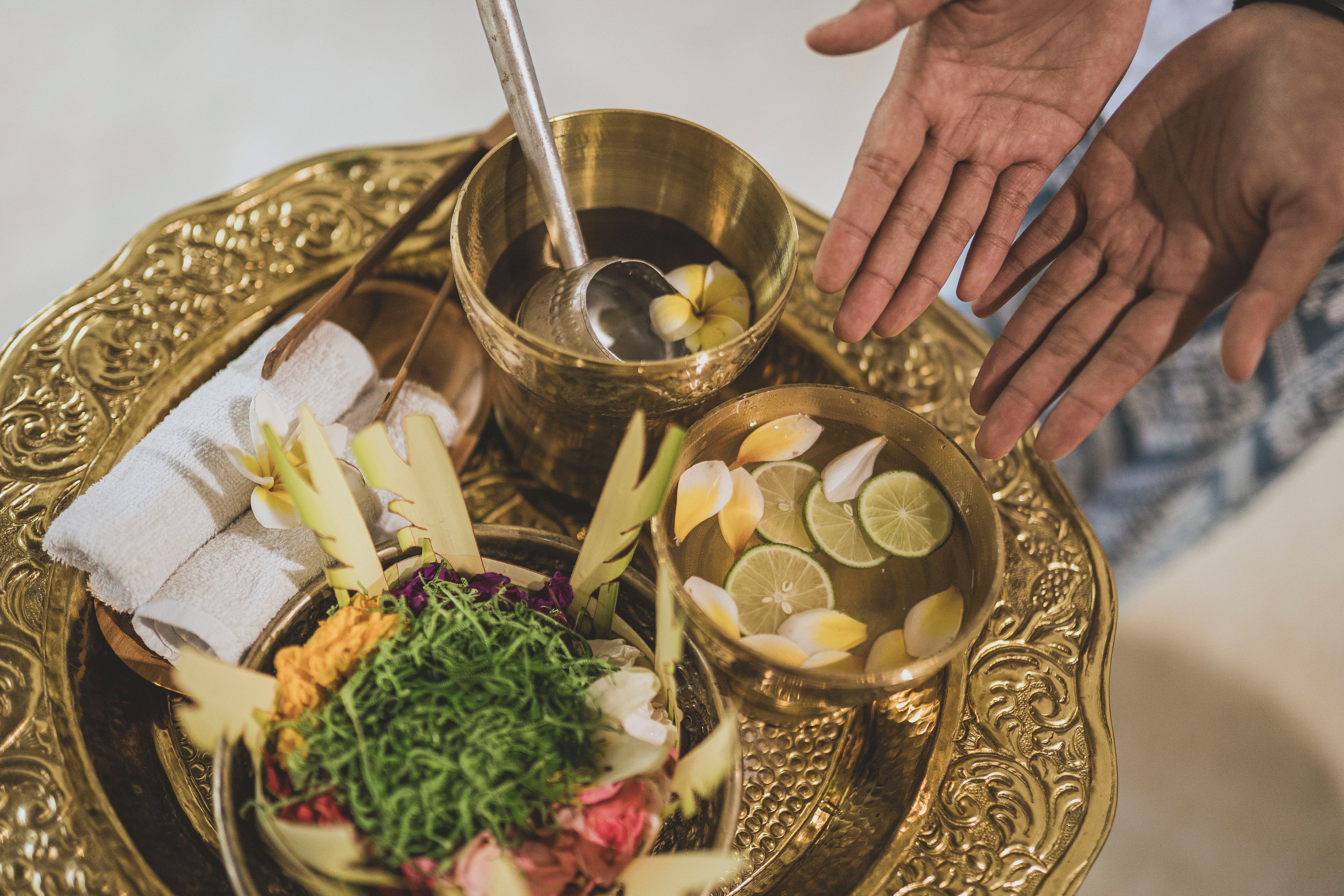A tray with a golden bowl containing slices of lime, a bowl of green herbs, and a white cloth.