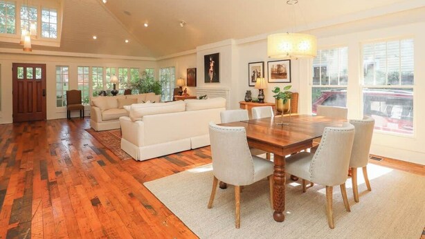 Ein geräumiges Wohnzimmer mit einem Holzespeisetisch, weißen Sofas und großen Fenstern.
