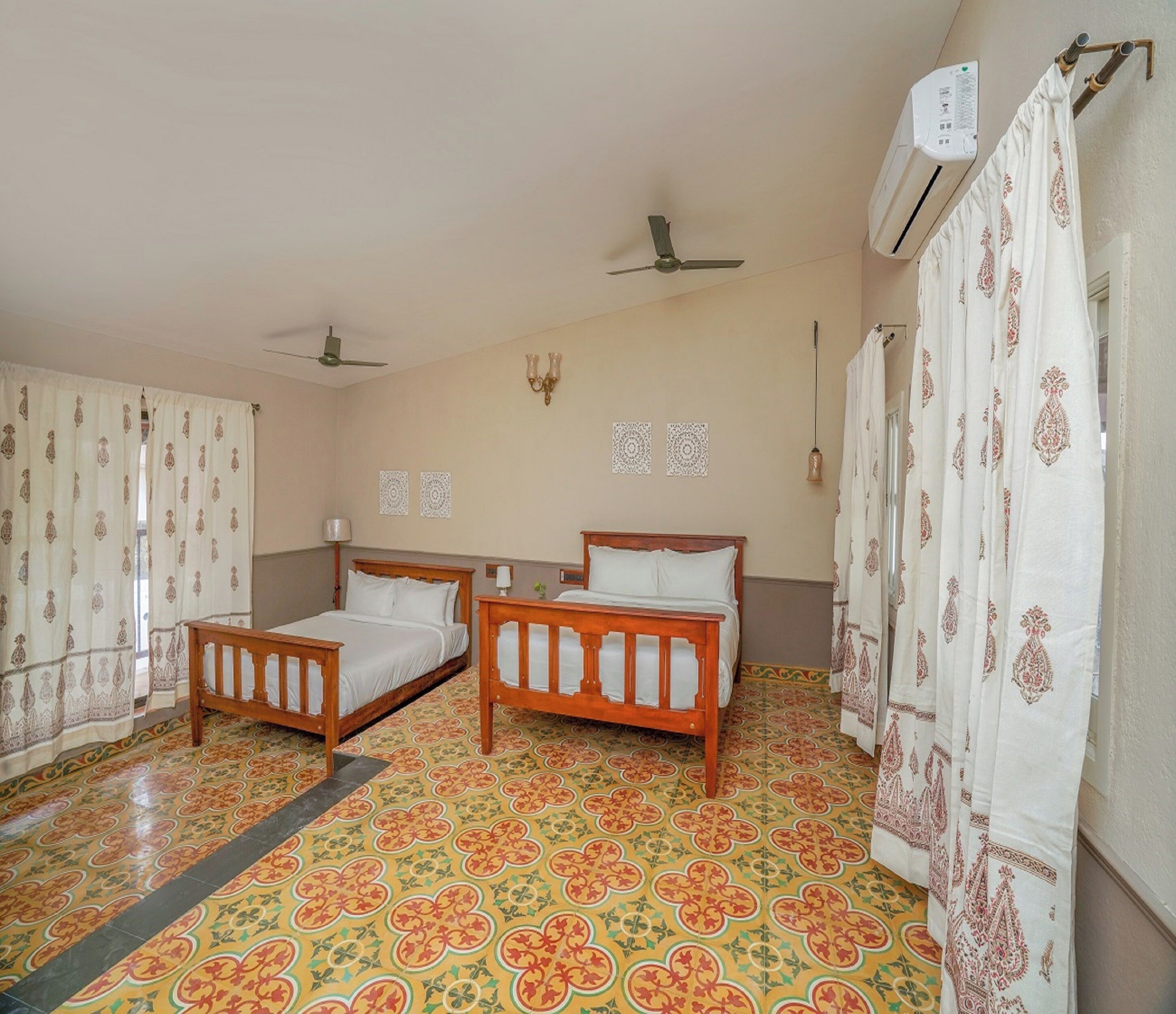 A room with two wooden beds, patterned curtains, a ceiling fan, and an air conditioning unit.