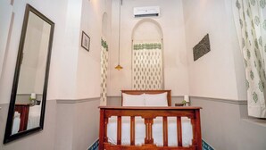 Un dormitorio con una cama de madera, ventilador de techo, aire acondicionado en la pared y cortinas estampadas.