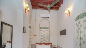 Un dormitorio con cama de madera, ventilador de techo, luces fijadas a la pared, un espejo y cortinas estampadas.