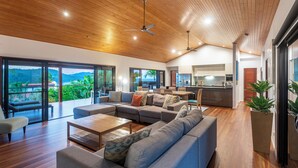 A spacious living area with a large sectional sofa, a wooden ceiling, and a view of a lush landscape.