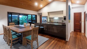 A modern kitchen with a large island, wooden dining table with chairs, and a view of the outdoors through large windows.