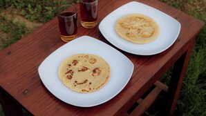 A wooden table with two white plates, each containing a pancake, and two glasses of a dark beverage.