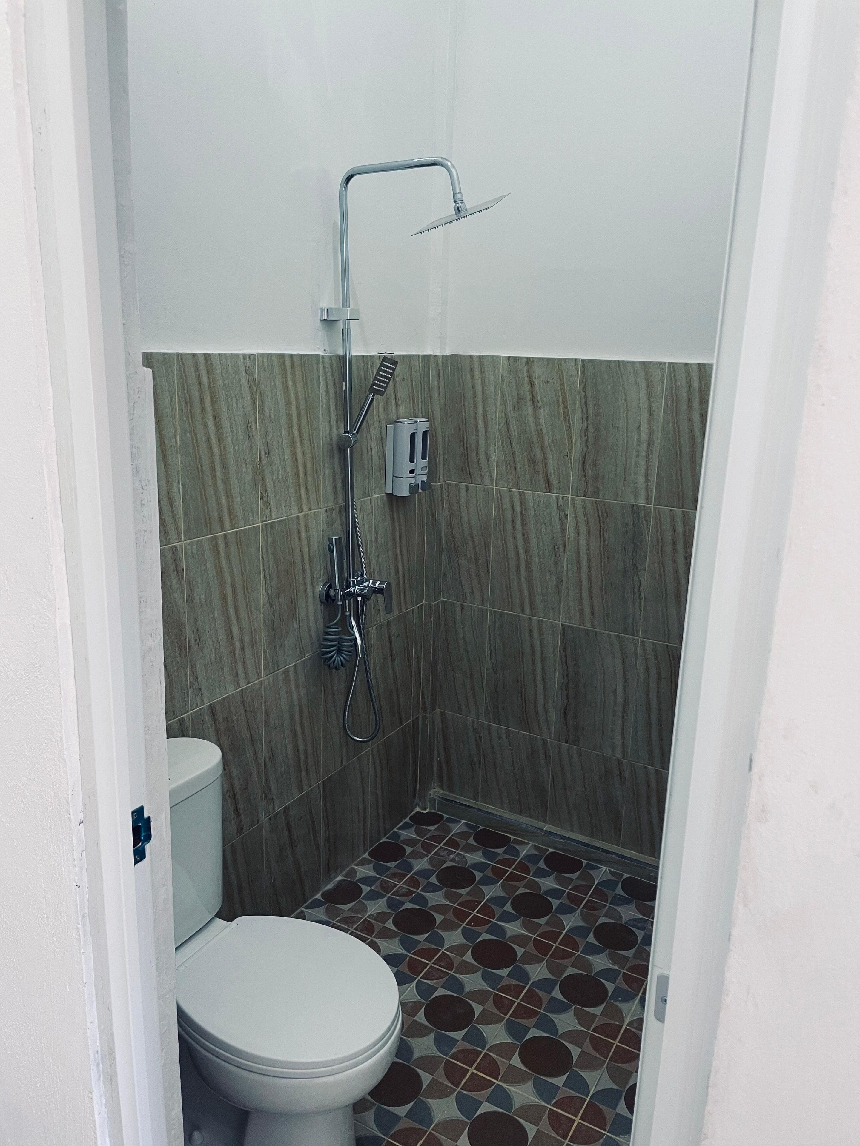Un baño pequeño con azulejos, ducha, inodoro y dispensador de jabón en la pared.