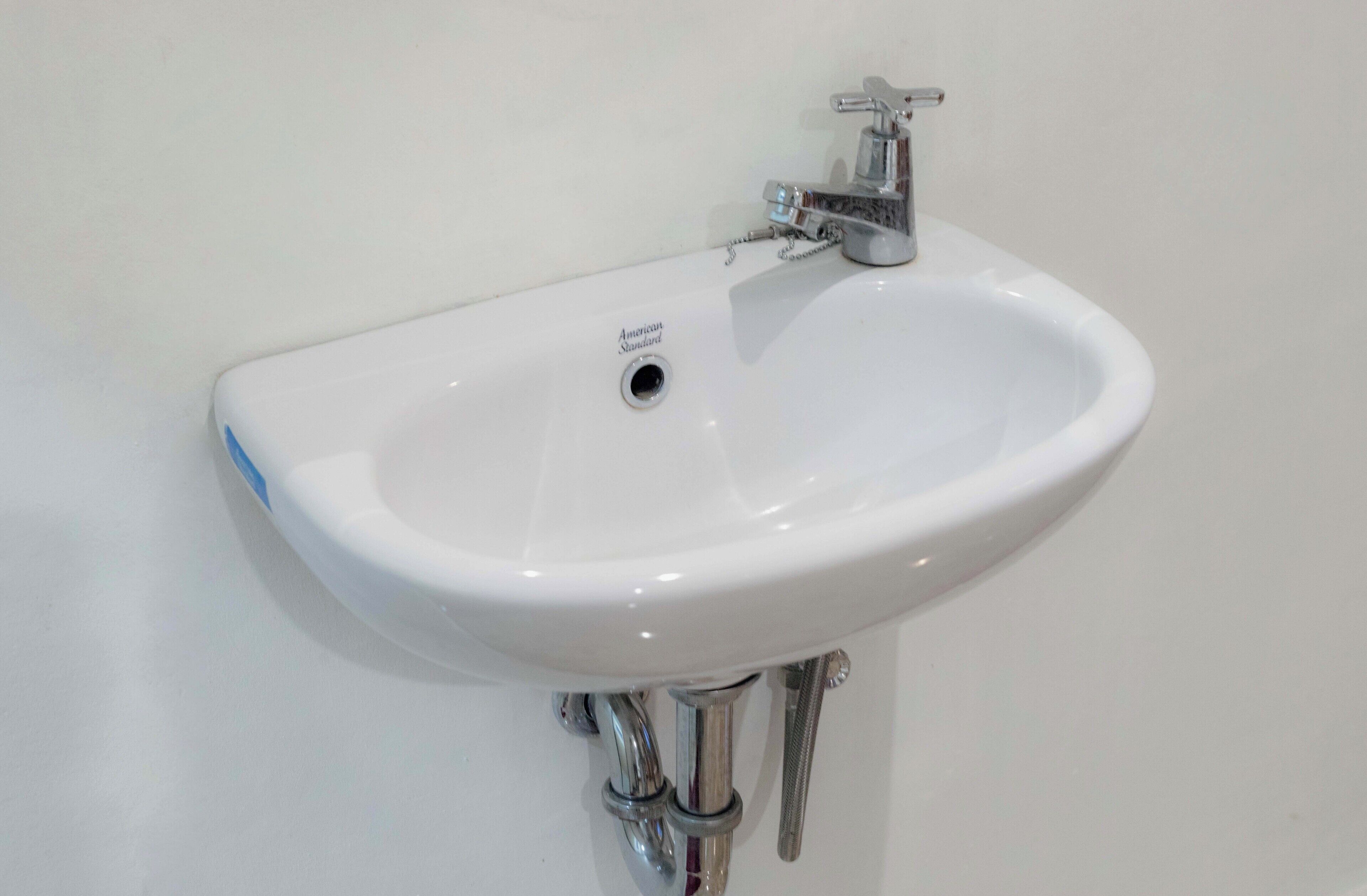 A white wall-mounted sink with a single faucet and a drain.