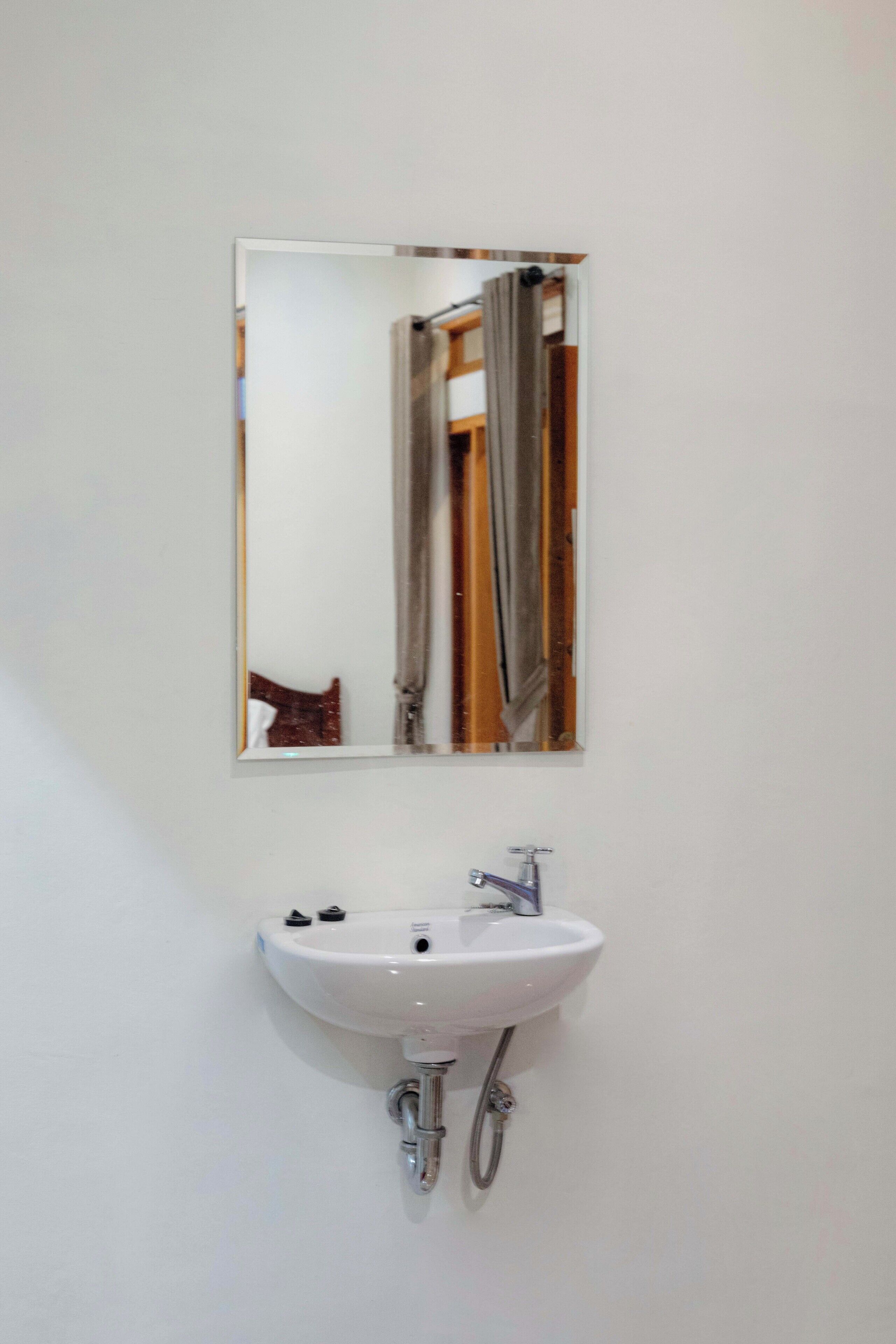 A white bathroom with a wall-mounted sink and a mirror above it.