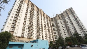 A high-rise residential building with multiple balconies and a parking area in front.