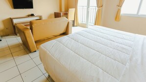 A hotel room with a large bed, a desk, a chair, and a television on the wall.