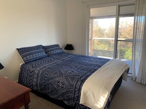 Une chambre avec un grand lit, une table de chevet, une fenêtre donnant sur des arbres et un balcon.