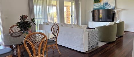 A modern living room with a sofa, TV, and dining area with chairs and a table.