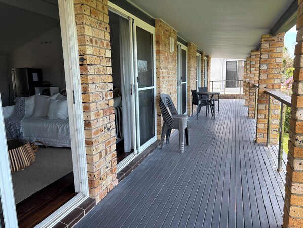 A covered outdoor area with a wooden deck, a sofa, and a table with chairs. - Beachfront house on beautiful One Mile Beach (Forster)