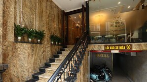 A marble staircase with a black railing, potted plants, and a sign reading 'LÔI VÀO XE MÁY' in a hotel lobby.