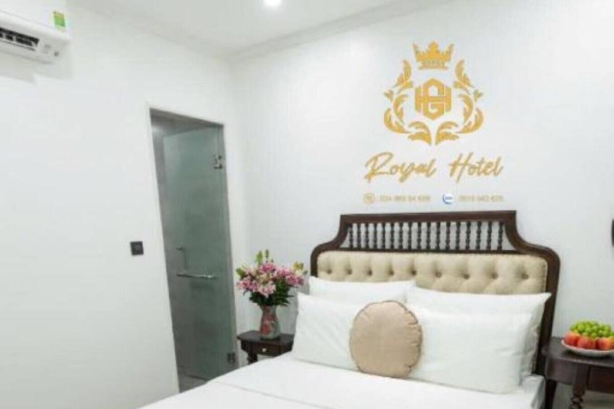 Una habitación de hotel con cama, mesita de noche, un florero con flores y una puerta.