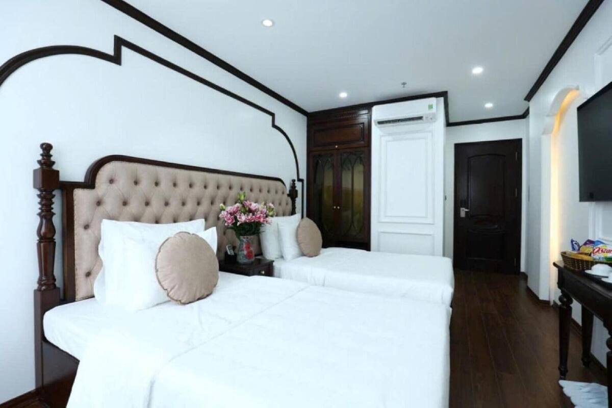Habitación de hotel con una cama grande, una mesita de noche con un jarrón de flores, un televisor y una puerta que da a otra habitación.