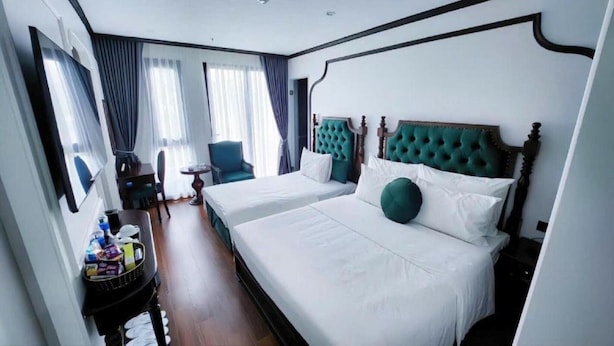 A hotel room with two beds, a chair, a small table, and a window with curtains.
