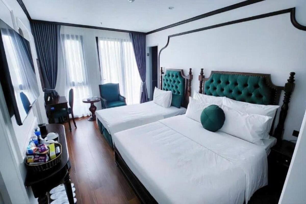 Habitación de hotel con dos camas, una silla, una mesita y un ventanal con cortinas.