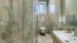 Un baño moderno con ducha de vidrio, un lavabo blanco y un inodoro.