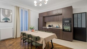 Una cocina moderna con armarios de madera oscura, horno empotrado y refrigerador. En la habitación contigua hay una mesa de comedor con sillas.