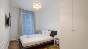 Un dormitorio moderno con cama, mesitas de noche, armario y un gran ventanal con cortinas.