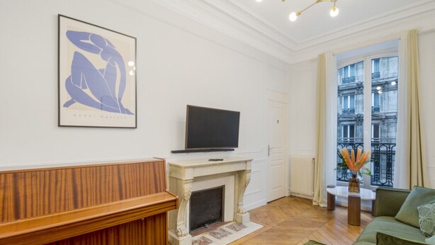 Una sala de estar con chimenea, televisor, sofá y ventana con vista a edificios.