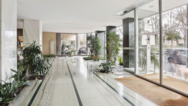 A modern lobby with a marble floor, glass doors, and indoor plants. - Bail mobilité - grand studio - Paris (Boulogne-Billancourt)
