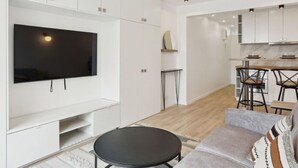 A modern living room with a flat-screen TV, a grey sofa, and a small black table. - Bail mobilité - grand studio - Paris (Boulogne-Billancourt)