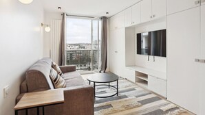 A modern living room with a sofa, a round coffee table, and a TV on a white cabinet. - Bail mobilité - grand studio - Paris (Boulogne-Billancourt)