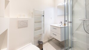 A modern bathroom with a glass shower enclosure, a white sink, and a towel rack.