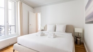 A hotel room with a large bed, two bedside lamps, a window with curtains, and a door.