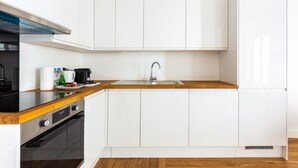 Une cuisine moderne avec des meubles blancs, un plan de travail en bois, un évier en acier inoxydable et une cuisinière noire.