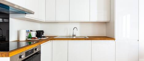 A modern kitchen with white cabinetry, a wooden countertop, a stainless steel sink, and a black stove.