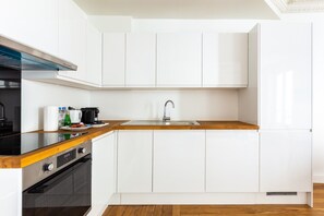 Une cuisine moderne avec des meubles blancs, un plan de travail en bois, un évier en acier inoxydable et une cuisinière noire.