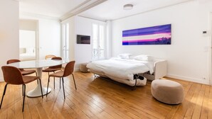 Une chambre à coucher moderne avec un lit, une table de chevet, une chaise, une petite table et un tableau accroché au mur.
