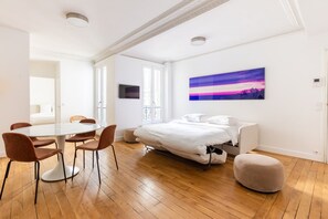 Une chambre à coucher moderne avec un lit, une table de chevet, une chaise, une petite table et un tableau accroché au mur.