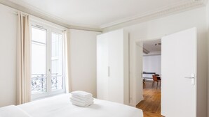 A hotel room with a bed, a balcony with curtains, and an open door leading to a dining area. - Eiffel Tower - Renovated 4 people (Paris)