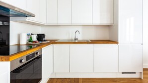 A modern kitchen with white cabinets, a wooden countertop, a stainless steel sink, and a built-in oven. - Eiffel Tower - Renovated 4 people (Paris)