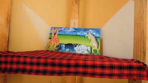 A room with a red plaid bedspread, a painting of giraffes and a zebra on the wall, and a wooden beam structure. - Sero Safaris Hostel (Arusha)
