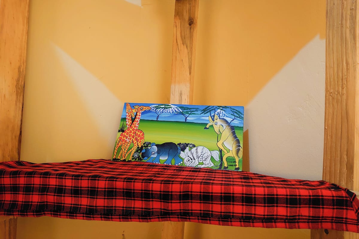 A room with a red plaid bedspread, a painting of giraffes and a zebra on the wall, and a wooden beam structure.