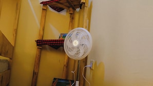 A corner room with a standing fan, a wooden ladder, and a red and black checkered cloth. - Sero Safaris Hostel (Arusha)