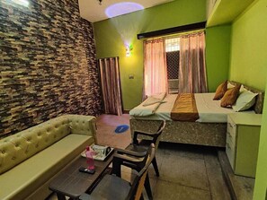 A compact room with a sofa, a small table, a bed with a mattress and pillows, and a nightstand. - Hotel Pearl By GRB (Patna)