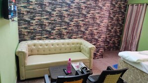 A room with a beige sofa, a small table with chairs, a bed, and a stone-patterned wall.
