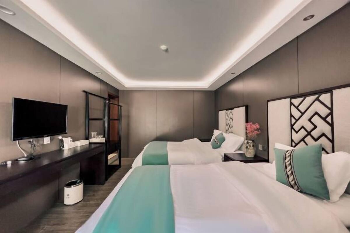 A modern hotel room with two beds, a desk, a flat-screen TV, and a mirror.