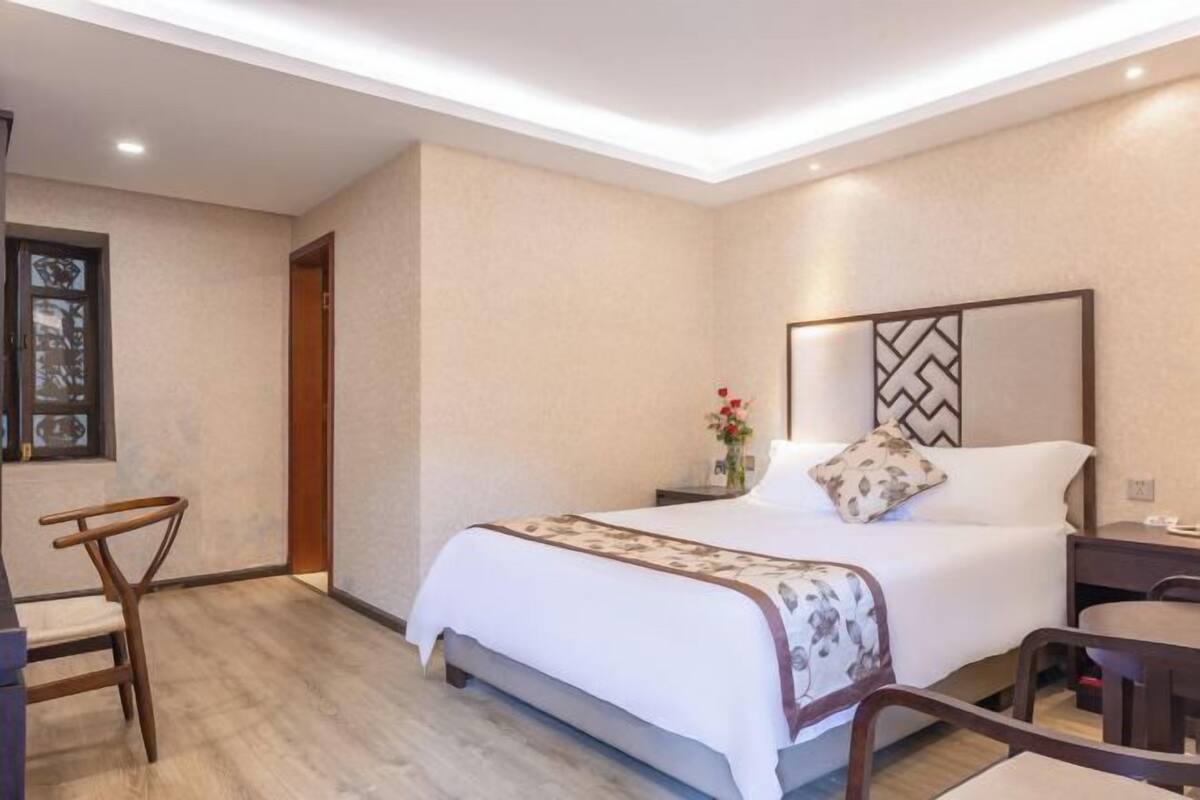 A hotel room with a bed, bedside table, chair, and a small desk with a chair.