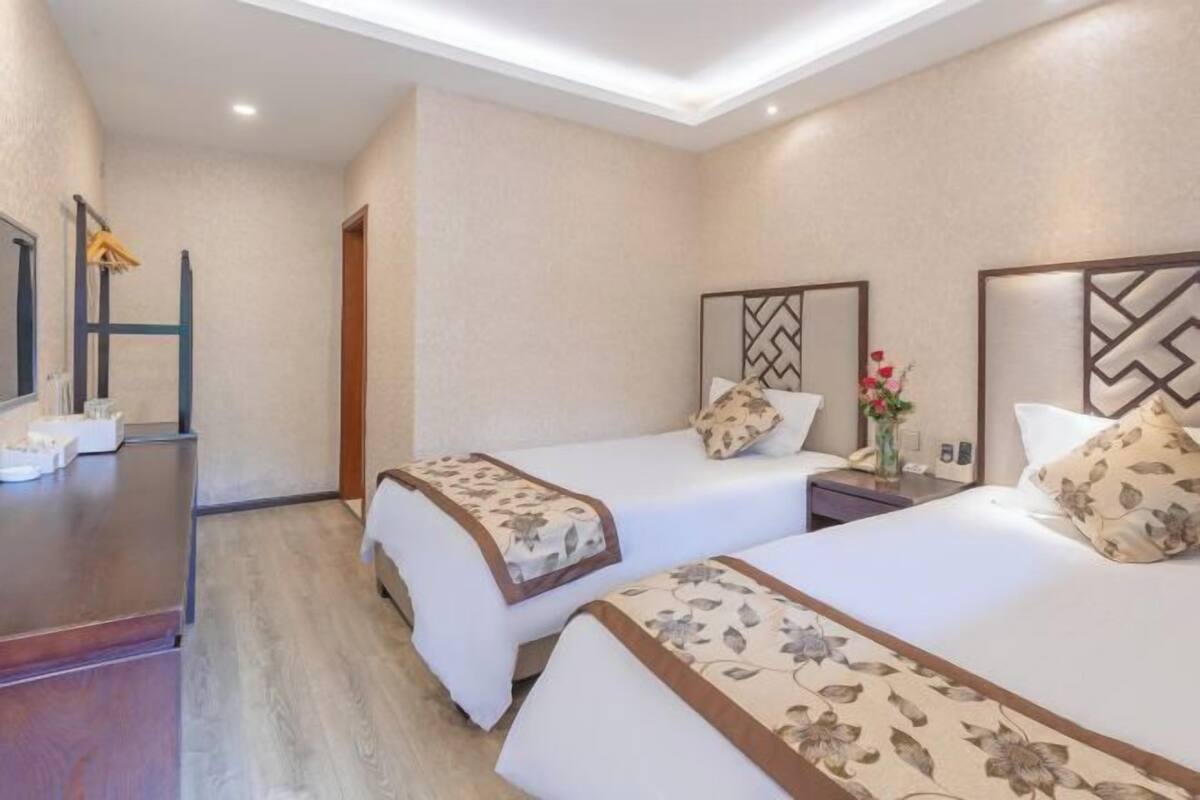 A hotel room with two beds, a desk, a chair, a nightstand, and a mirror.
