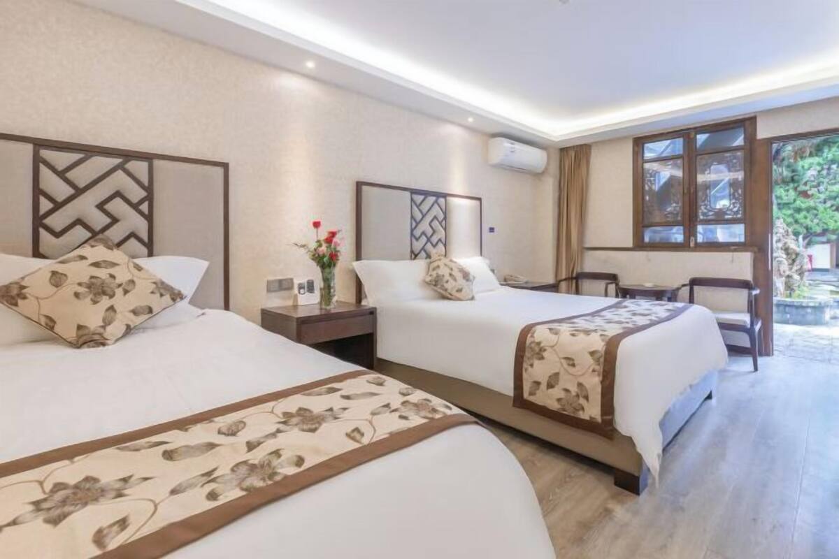A hotel room with two beds, a desk, a chair, and a window with a view.