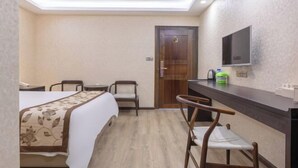 A hotel room with a bed, a desk, two chairs, a television, and a door. - Yahve Academy Hotel (Dali City)